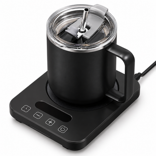 Black coffee mug with clear lid and metal straw on the matching black electric mug warmer, white background