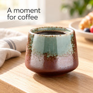 Grün-braune 200-ml-Keramiktasse mit Kaffee auf einer hölzernen Frühstückstheke