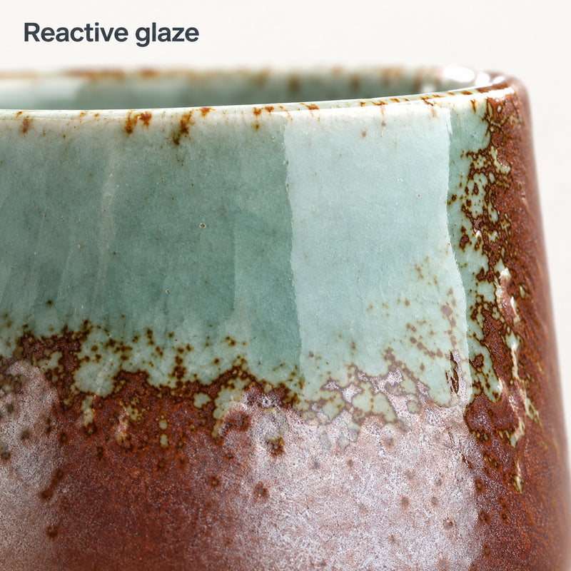 Nahaufnahme der seladongrünen, zartmauvefarbenen und braunen Reaktionsglasur auf der Kaffeetasse aus Keramik
