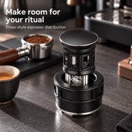 Black press-style espresso distributor beside a portafilter and coffee cup at a home coffee station.