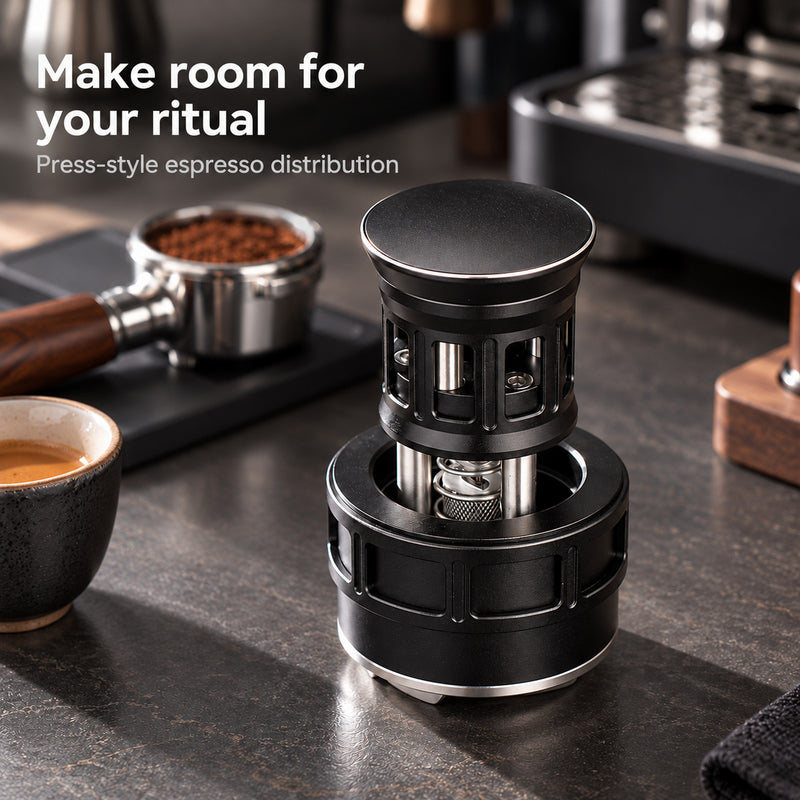 Black press-style espresso distributor beside a portafilter and coffee cup at a home coffee station.