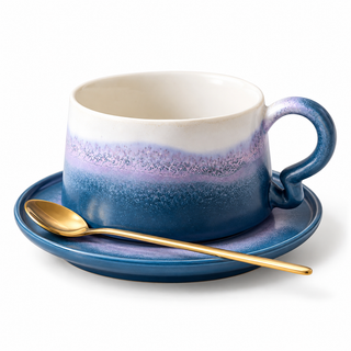 Keramik-Kaffeetasse mit blau-lavendelfarbenem Verlauf auf passender Untertasse mit goldfarbenem Löffel vor weißem Hintergrund