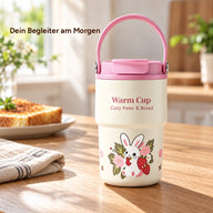 Rosa Becher mit Keramikbeschichtung und Hasen-, Erdbeer- und Blumenmotiv auf einem Frühstückstisch