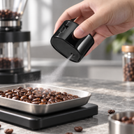 Hand besprüht geröstete Bohnen in einer Metallschale auf einer Kaffeewaage mit dem schwarzen Kaffeebohnen-Zerstäuber