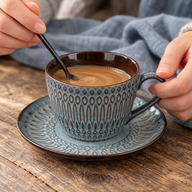 Milk coffee being stirred in the blue-gray ceramic cup on its matching saucer