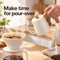 Ivory white gooseneck kettle pouring water into a paper-lined coffee dripper in a home kitchen.