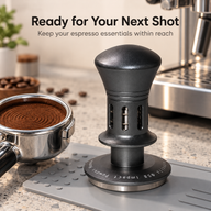 Gunmetal espresso tamper on a tamping mat beside a coffee-filled portafilter
