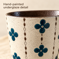 Primo piano di fiori verde acqua, catene di rombi marroni e ceramica crema puntinata sulla tazza Fiori verde acqua.