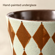 Close-up of the hand-painted rust-brown diamond pattern and textured pale mint ceramic glaze.