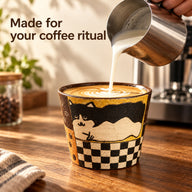 Skummad mjölk hälls i kaffekoppen i keramik med kattmönster