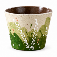 Henkellose Keramik-Kaffeetasse mit Wiesenmuster, grünem Laub und weißen Zweigen auf weißem Hintergrund.