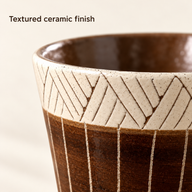 Macro view of the cream chevron band and brown vertically lined ceramic cup surface