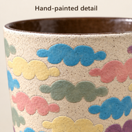 Close-up van de pastelkleurige wolkenmotieven en fijne stipjes op de wand van een keramische kop.