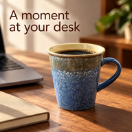 Mottled blue ceramic coffee mug filled with coffee beside a laptop and notebook