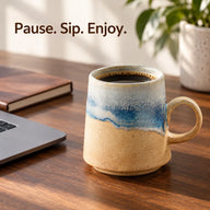 Blue and sand ceramic mug filled with coffee beside a laptop and notebook