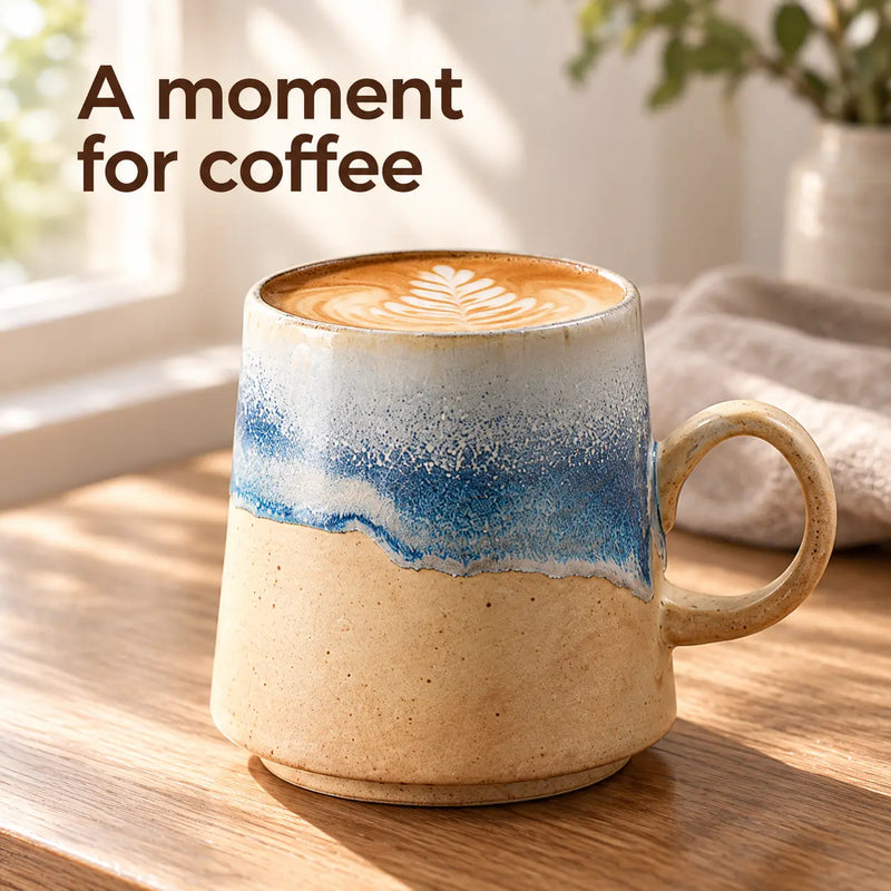 Blue and sand ceramic coffee mug filled with latte on a sunlit wooden table