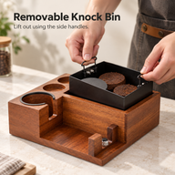 Black metal knock bin being lifted from the sapele wood espresso station using its two side handles.