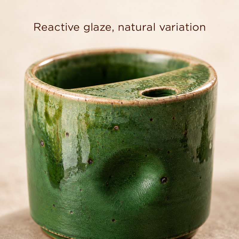 Close-up of the green reactive glaze and thumb indentation on the small ceramic cup.