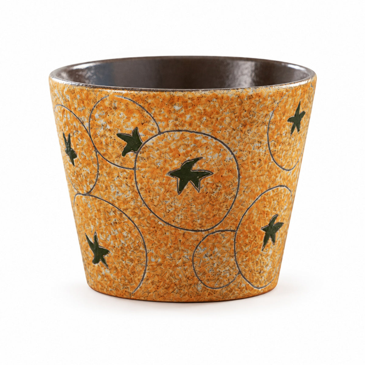 Tazza da caffè in ceramica color ambra senza manico con stelle verdi e cerchi delineati, vuota su sfondo bianco.