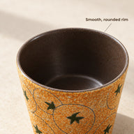 Primo piano del bordo scuro arrotondato e dell'interno smaltato marrone della tazza in ceramica senza manico.