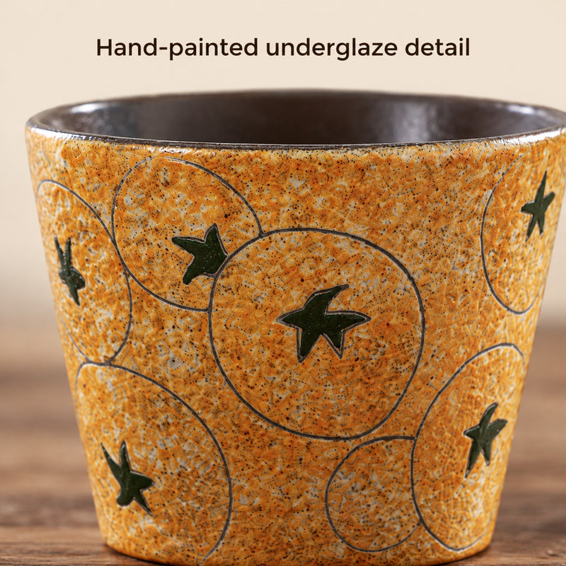 Primo piano di stelle verdi, sottili cerchi delineati e decoro sottosmalto ambra puntinato sulla tazza in ceramica.