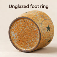 Fondo della tazza in ceramica con base ambra puntinata circondata da un anello d'appoggio scuro non smaltato.