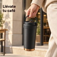 Taza de café negro mate llevada por su asa plegable delante de una cafetería