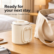 Compact cream kettle with the handle folded flat beside a travel tote in a hotel room.