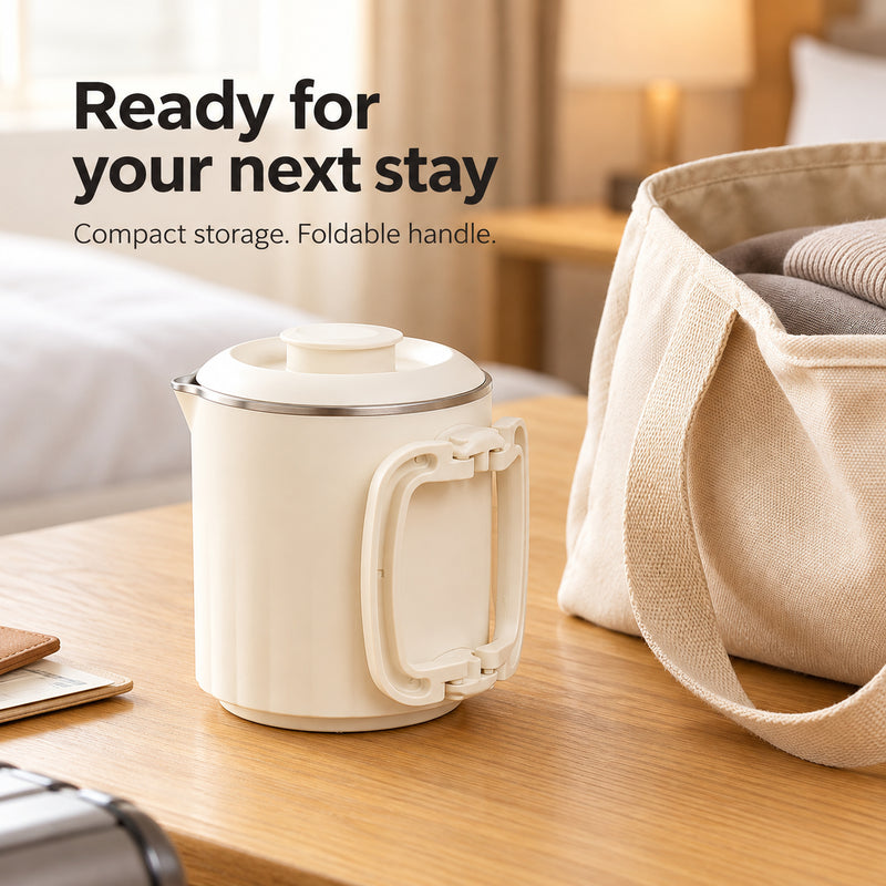 Compact cream kettle with the handle folded flat beside a travel tote in a hotel room.