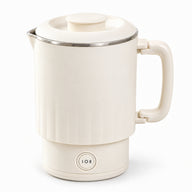 Cream 800 mL travel electric kettle on its heating base with the folding handle open, shown on white.