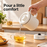 Hand pouring water from the cream travel kettle into a glass tea cup, with the heating base on the counter.