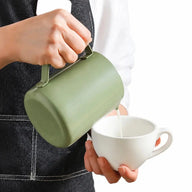 Pichet à dégradé vert versant du lait chauffé à la vapeur dans une tasse