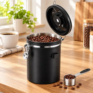 Recipiente negro abierto de acero inoxidable con granos de café y la cuchara medidora al lado