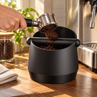 Black Large espresso knock box receiving a used coffee puck at an espresso station