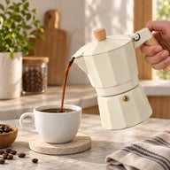 Cream moka pot pouring coffee into a white cup