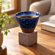 Deep Blue ceramic coffee cup with black coffee in its square base beside a reading chair
