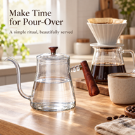 Clear glass gooseneck kettle beside a pour-over dripper and coffee server in a bright kitchen