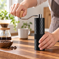 Hand turning the black Yozcoffee manual coffee grinder beside a pour-over coffee setup