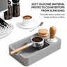 Gray silicone tamping mat holding a portafilter with grounds beside a tamper and distributor on an espresso counter