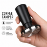 Hand holding a black espresso tamper with a polished stainless base and concentric leveling rings